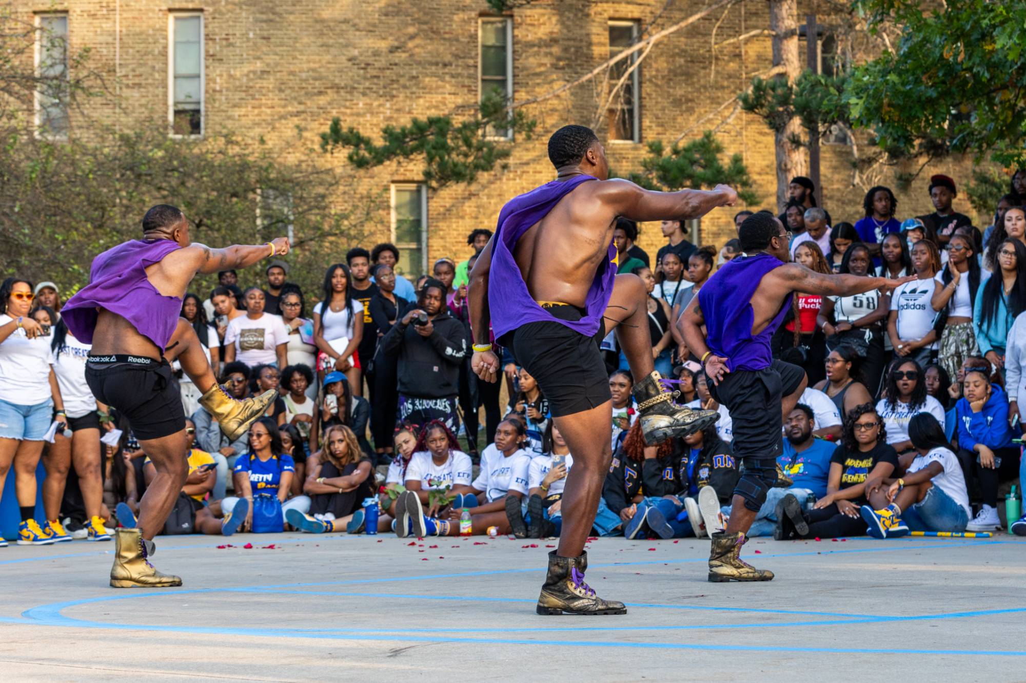 three male students dancing in front of crowd of students